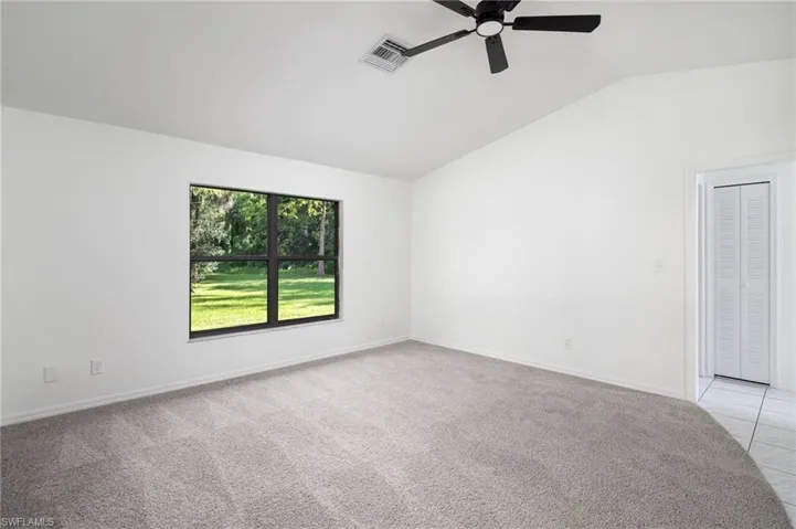 Living room featuring new light colored carpet, vaulted ceiling, and ceiling fan with view of back yard.