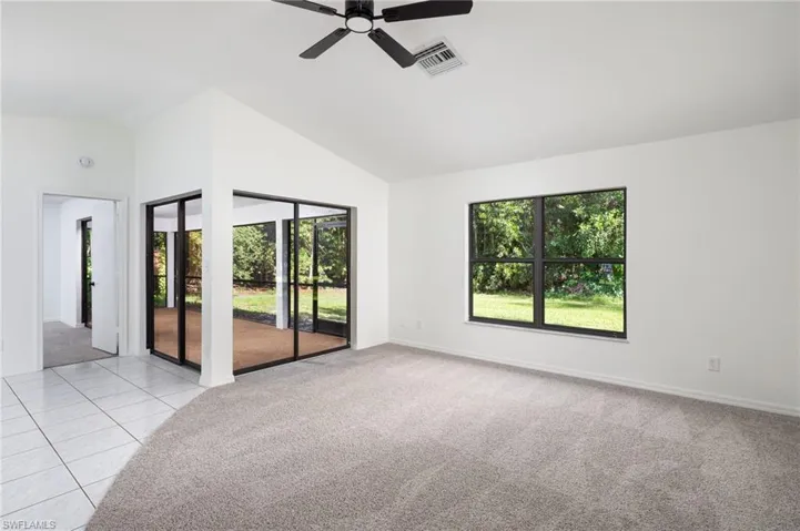 Living room featuring healthy amount of natural light, light carpet, lofted ceiling, ceiling fan, and light tile patterned flooring with access and view of back yard.