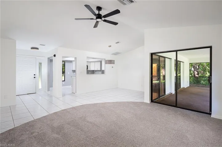View of dining area and kitchen from living room featuring light tile patterned flooring, lofted ceiling, light carpet, and ceiling fan