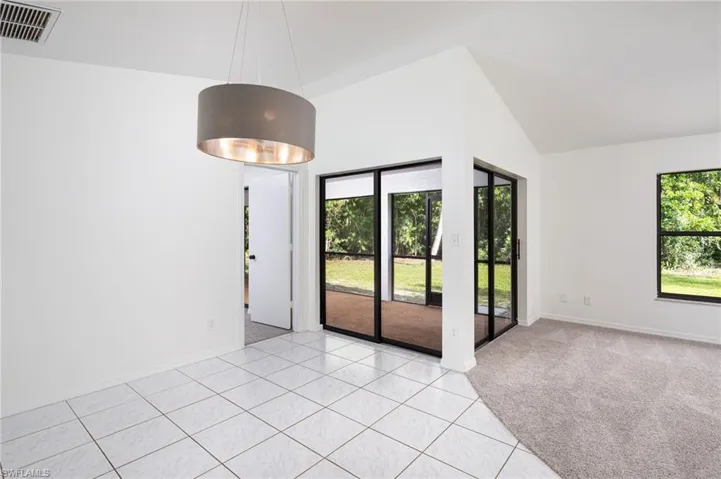 Dining room featuring light carpet, light tile patterned floors, and high vaulted ceiling and view of back yard