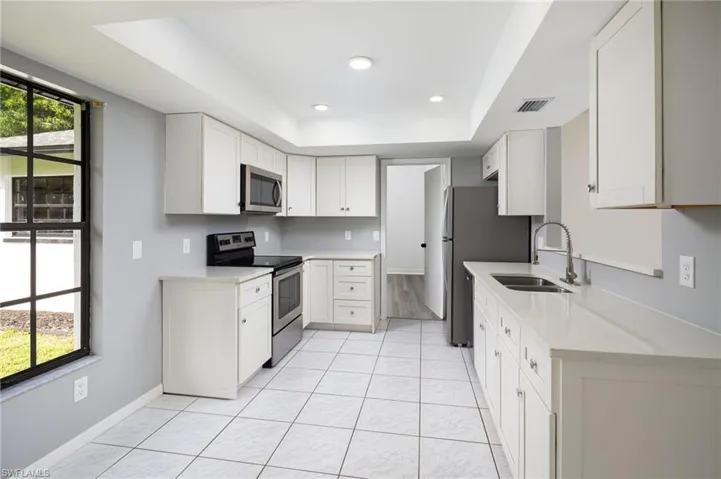 Kitchen with appliances with stainless steel finishes, a raised ceiling, white cabinetry, quartz countertops, and recessed lighting