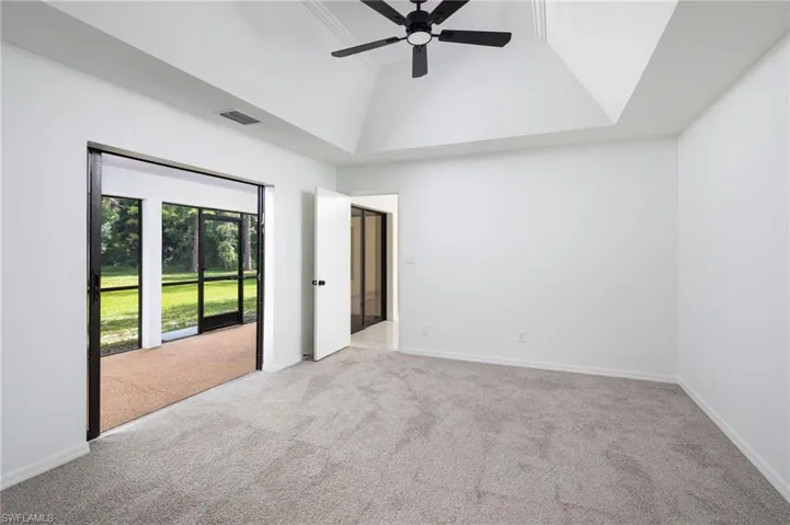 Unfurnished bedroom with access to outside, light colored carpet, a tray ceiling, and a ceiling fan