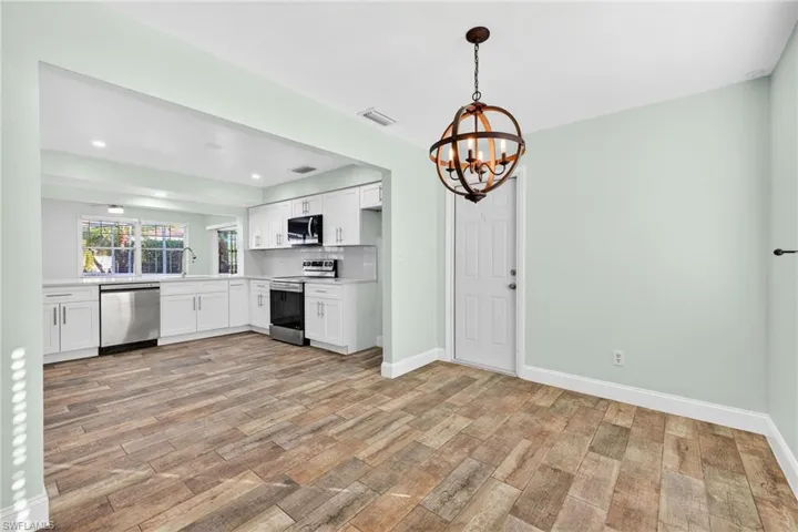 Kitchen with white cabinets, light countertops, stainless steel appliances, a chandelier, and light wood-style floors