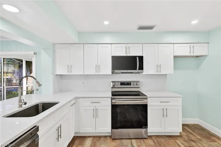 Kitchen featuring stainless steel appliances, white cabinetry, light stone counters, light wood-type flooring, and recessed lighting