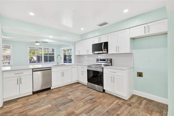 Kitchen with white cabinetry, appliances with stainless steel finishes, light wood-type flooring, decorative backsplash, and recessed lighting