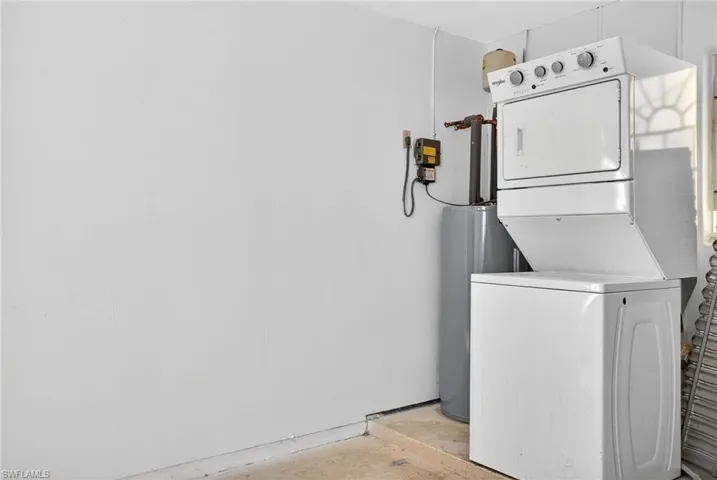 Laundry area featuring stacked washer and clothes dryer, water heater, and unfinished concrete floors