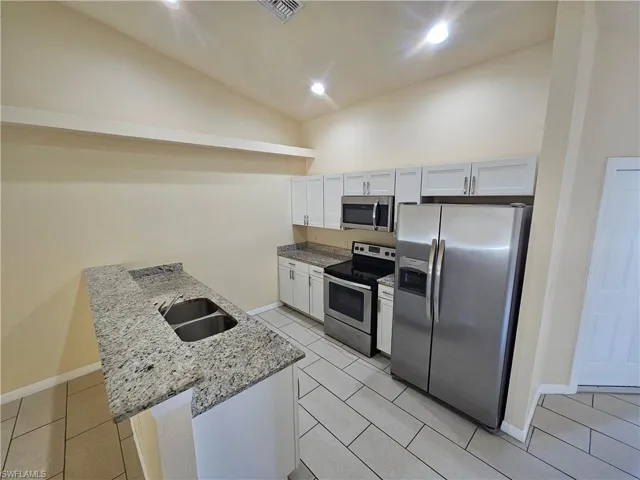 Kitchen featuring lofted ceiling, light stone countertops, stainless steel appliances, a peninsula, and light tile patterned flooring