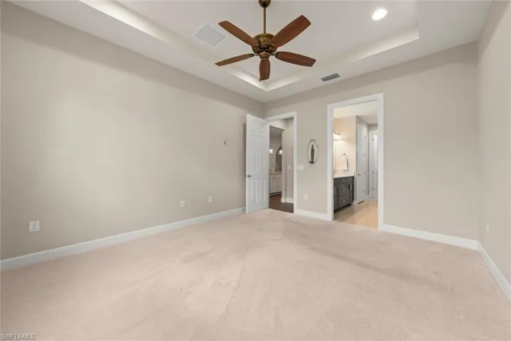 Master bedroom featuring light carpet, ceiling fan, a tray ceiling, and ensuite bath