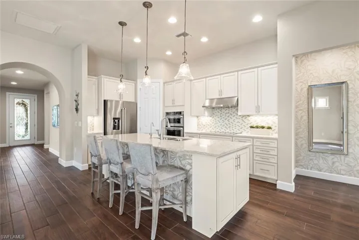 Kitchen with arched walkways, a breakfast Area  bar area, stainless steel appliances, light quartz  counters, and white cabinetry