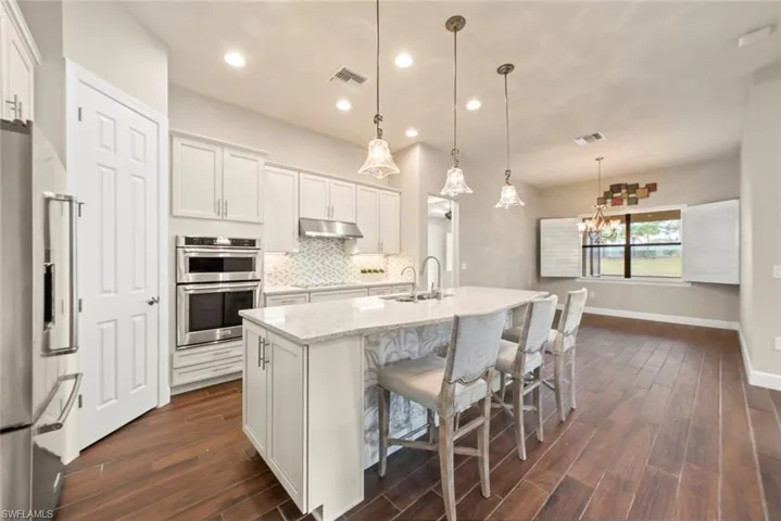 Kitchen with white cabinets, light quartz  counters, stainless steel appliances, a kitchen appliances,  breakfast bar, and dark tile flooring