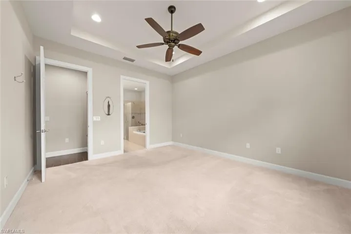 Master  bedroom featuring light colored carpet, a raised ceiling, recessed lighting, a ceiling fan, and ensuite bathroom