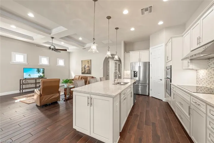 Kitchen with decorative backsplash, white cabinets, a ceiling fan, decorative light fixtures, and arched walkways
