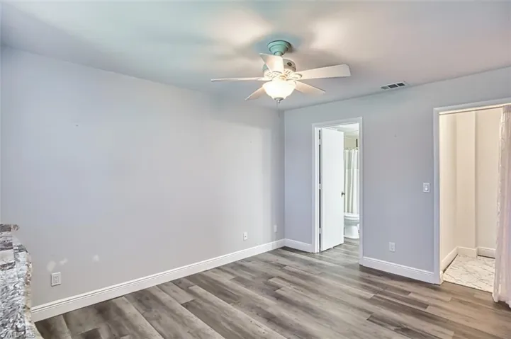 Unfurnished bedroom with dark wood-style flooring, ceiling fan, and connected bathroom