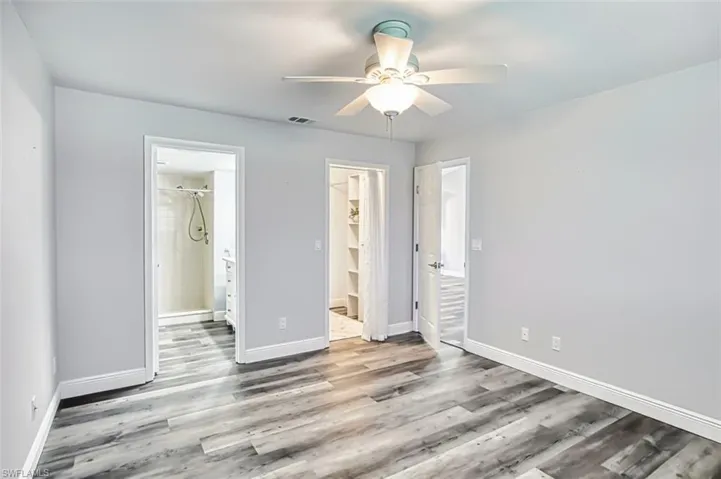 Unfurnished bedroom featuring ensuite bathroom, light wood-type flooring, a walk in closet, and a ceiling fan