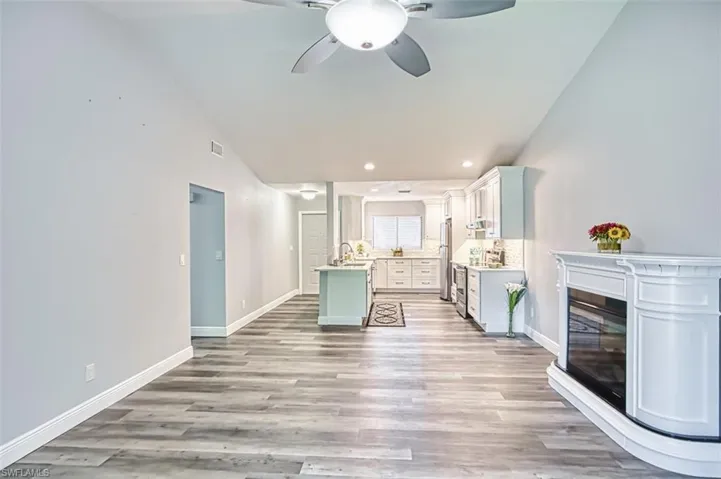 Living room with light wood-type flooring, recessed lighting, a ceiling fan, high vaulted ceiling, and a glass covered fireplace