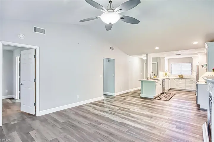 Kitchen featuring lofted ceiling, white cabinets, a center island with sink, ceiling fan, and light wood finished floors