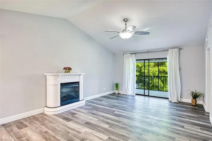 Unfurnished living room with a glass covered fireplace, lofted ceiling, light wood-style flooring, and a ceiling fan