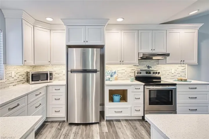 Kitchen featuring appliances with stainless steel finishes, decorative backsplash, under cabinet range hood, light stone counters, and light wood finished floors