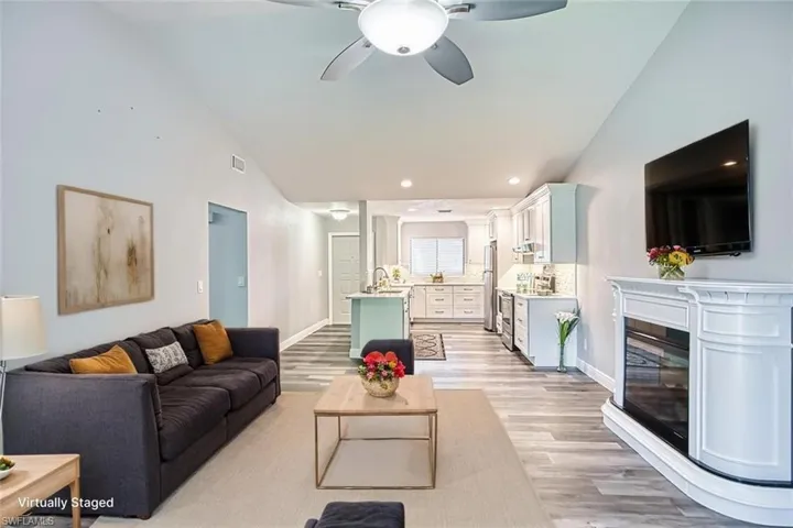 Living area with light wood-style floors, a glass covered fireplace, a ceiling fan, recessed lighting, and high vaulted ceiling *VIRTUALLY STAGED