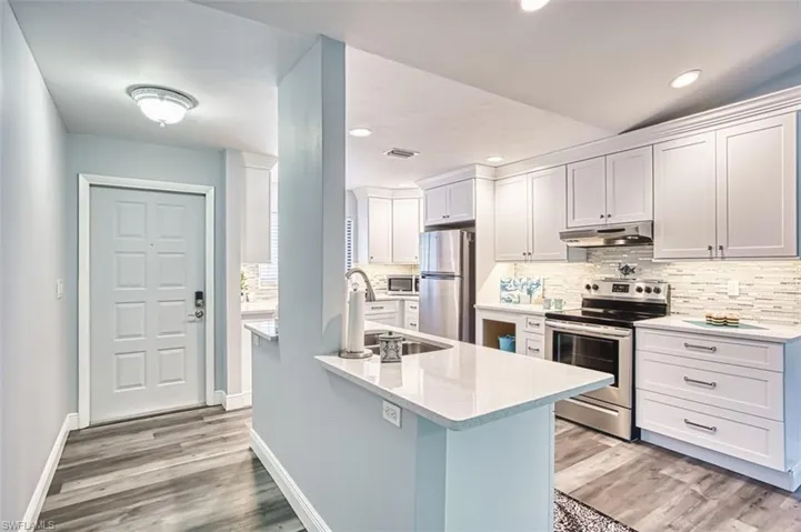 Kitchen featuring appliances with stainless steel finishes, light stone countertops, light wood finished floors, tasteful backsplash, and recessed lighting