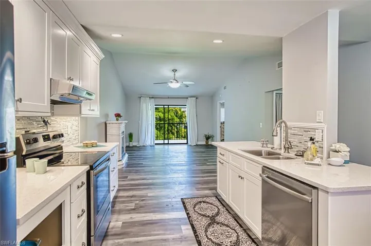 Kitchen with decorative backsplash, stainless steel appliances, white cabinets, light stone counters, and vaulted ceiling