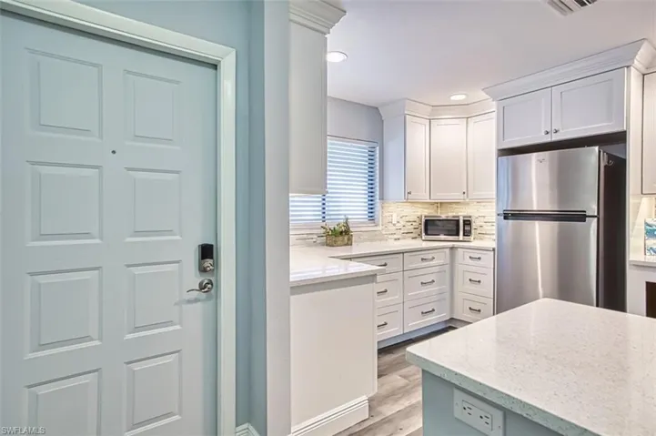 Kitchen with stainless steel appliances, light stone counters, white cabinets, decorative backsplash, and light wood-style floors