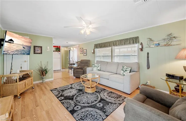 Living room with crown molding, a ceiling fan, wood finished floors, and baseboards