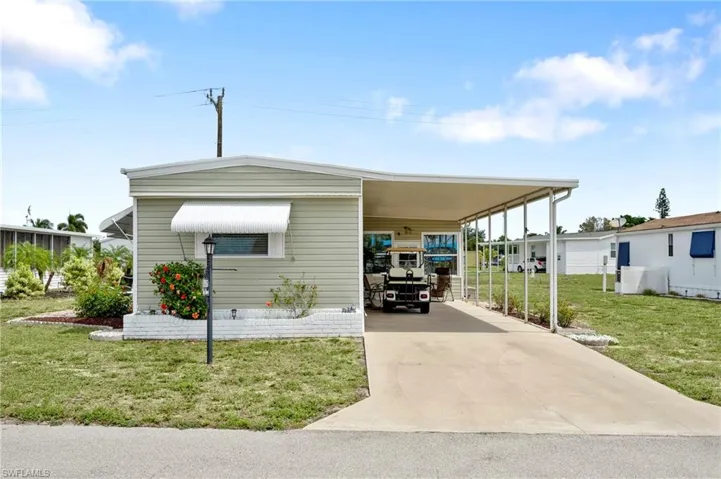 View of front of house featuring an attached carport, a front yard, and driveway