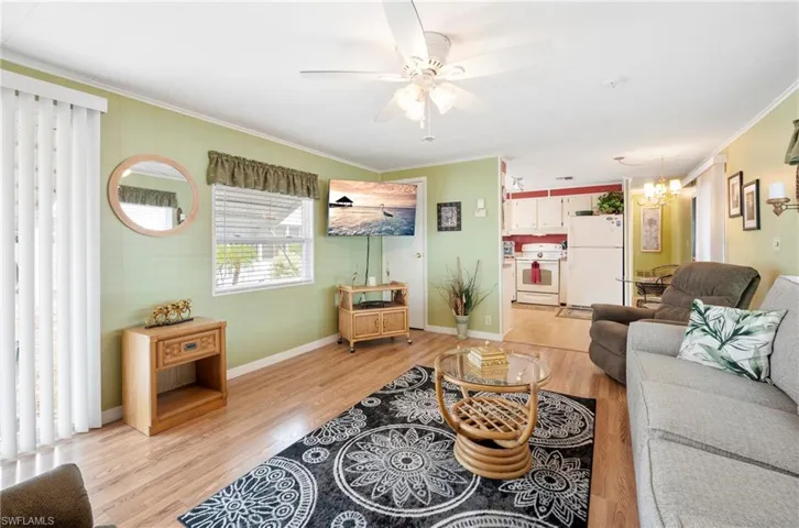 Living room featuring crown molding, light wood finished floors, ceiling fan, a chandelier, and baseboards