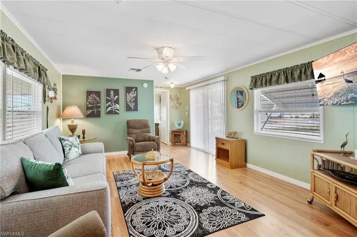 Living room with healthy amount of natural light, wood finished floors, baseboards, a ceiling fan, and crown molding