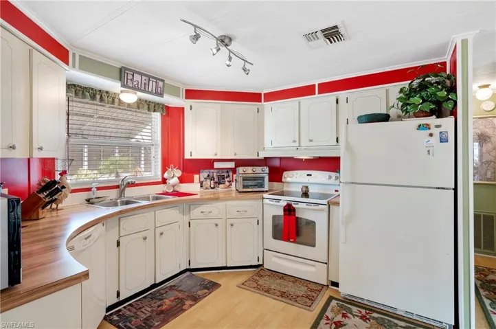 Kitchen with white appliances, under cabinet range hood, light wood-type flooring, light countertops, and a sink