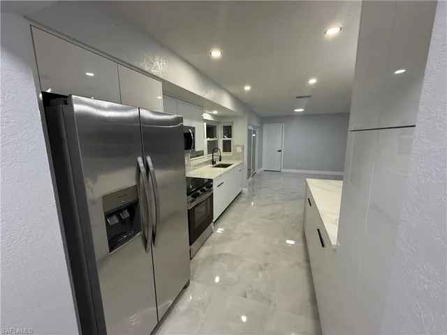 Kitchen with stainless steel appliances, modern cabinets, a textured wall, white cabinets, and light stone counters