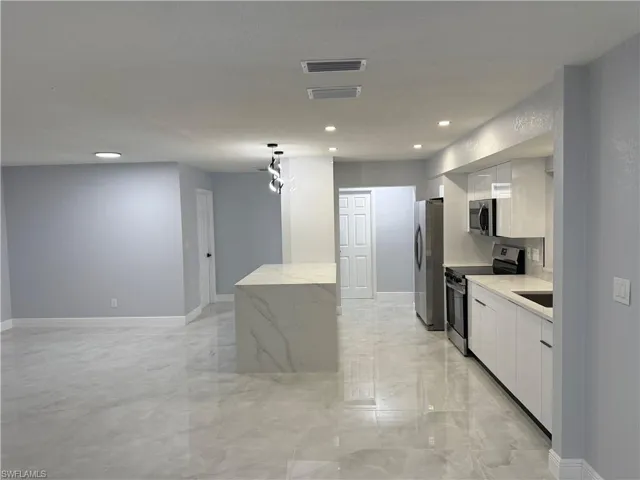Kitchen with white cabinets, stainless steel appliances, light stone countertops, light marble finish floors, and recessed lighting