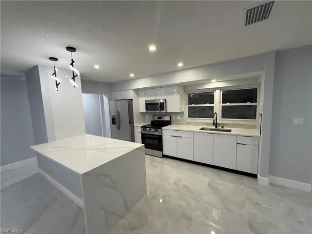 Kitchen featuring stainless steel appliances, white cabinetry, pendant lighting, light stone counters, and a textured ceiling