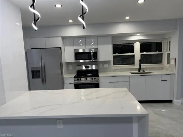 Kitchen featuring stainless steel appliances, light stone counters, modern cabinets, recessed lighting, and white cabinetry