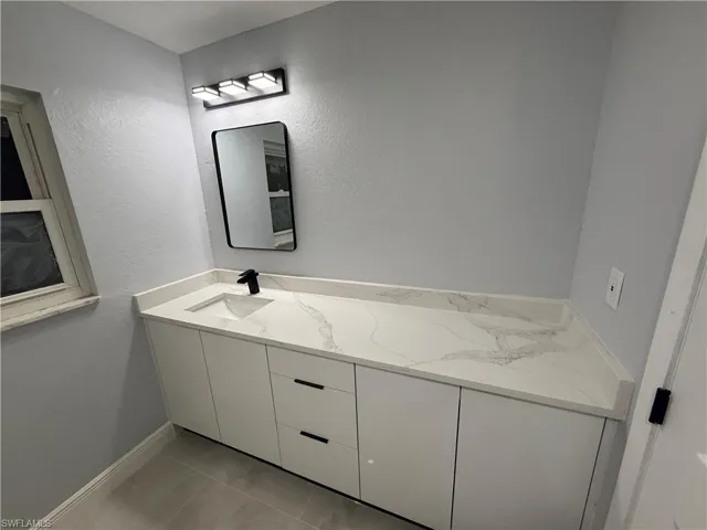 Bathroom with vanity, light tile patterned floors, and a textured wall