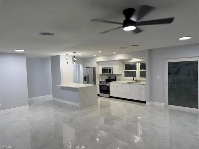 Kitchen with stainless steel appliances, white cabinetry, a ceiling fan, pendant lighting, and light stone counters