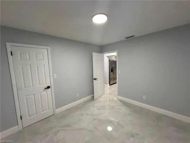 Unfurnished bedroom with stainless steel refrigerator with ice dispenser and light marble finish flooring