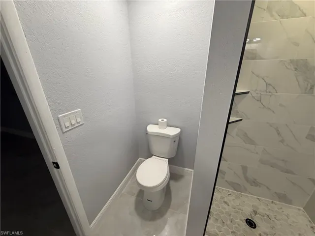 Bathroom with a shower stall, a textured wall, and light tile patterned flooring