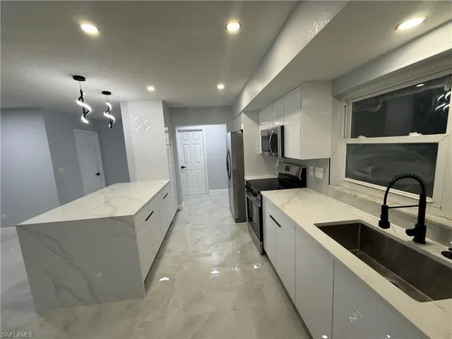 Kitchen featuring stainless steel appliances, recessed lighting, white cabinets, light stone counters, and light marble finish floors