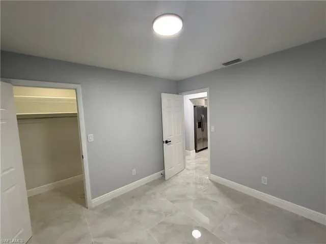 Unfurnished bedroom with a spacious closet and stainless steel fridge with ice dispenser