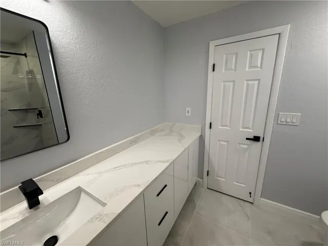 Full bathroom featuring vanity, a textured wall, a marble finish shower, and light marble finish floors