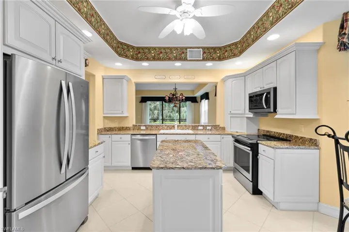 Kitchen with appliances with stainless steel finishes, a chandelier, light stone countertops, a tray ceiling, and recessed lighting
