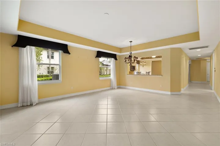 Empty room with a chandelier, a raised ceiling, and light tile patterned floors