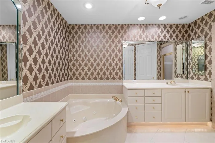 Full bathroom with two vanities, a tub with jets, wallpapered walls, recessed lighting, and light tile patterned floors