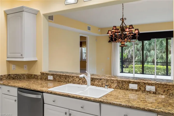 Kitchen with dark stone counters, dishwasher, decorative light fixtures, and white cabinets