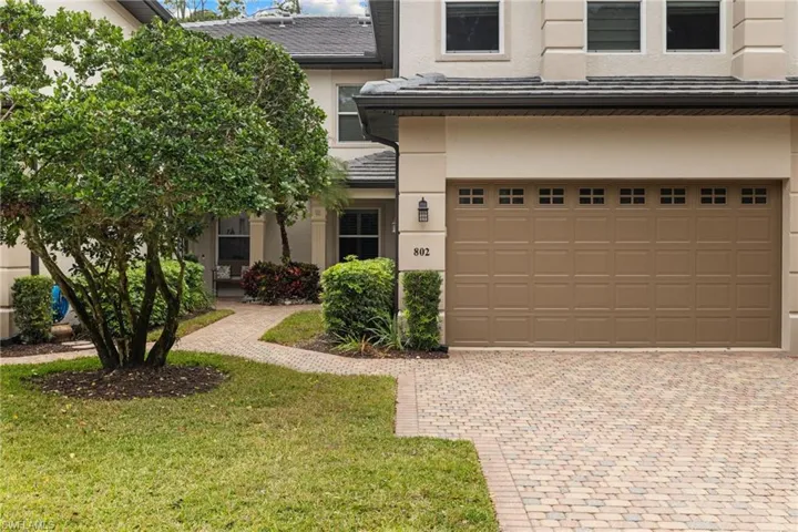 View of front of house with stucco siding, an attached garage, a front lawn, and decorative driveway