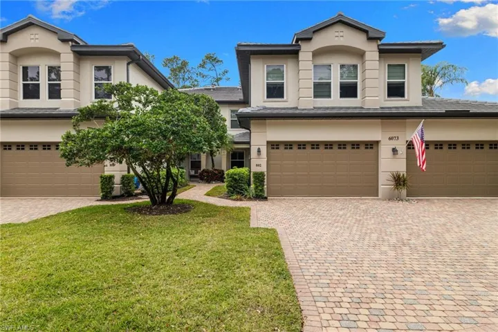 Traditional home featuring an attached garage, stucco siding, decorative driveway, and a front lawn