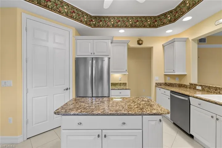 Kitchen with appliances with stainless steel finishes, white cabinetry, a ceiling fan, dark stone counters, and a kitchen island