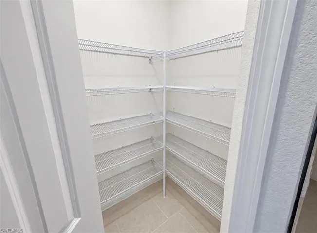 Corner pantry with wire shelving, textured wall finish, and tile flooring